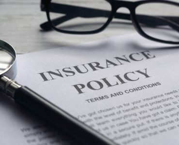 Selective focus of magnifying glass,glasses and Insurance Policy letter on a white wooden background.